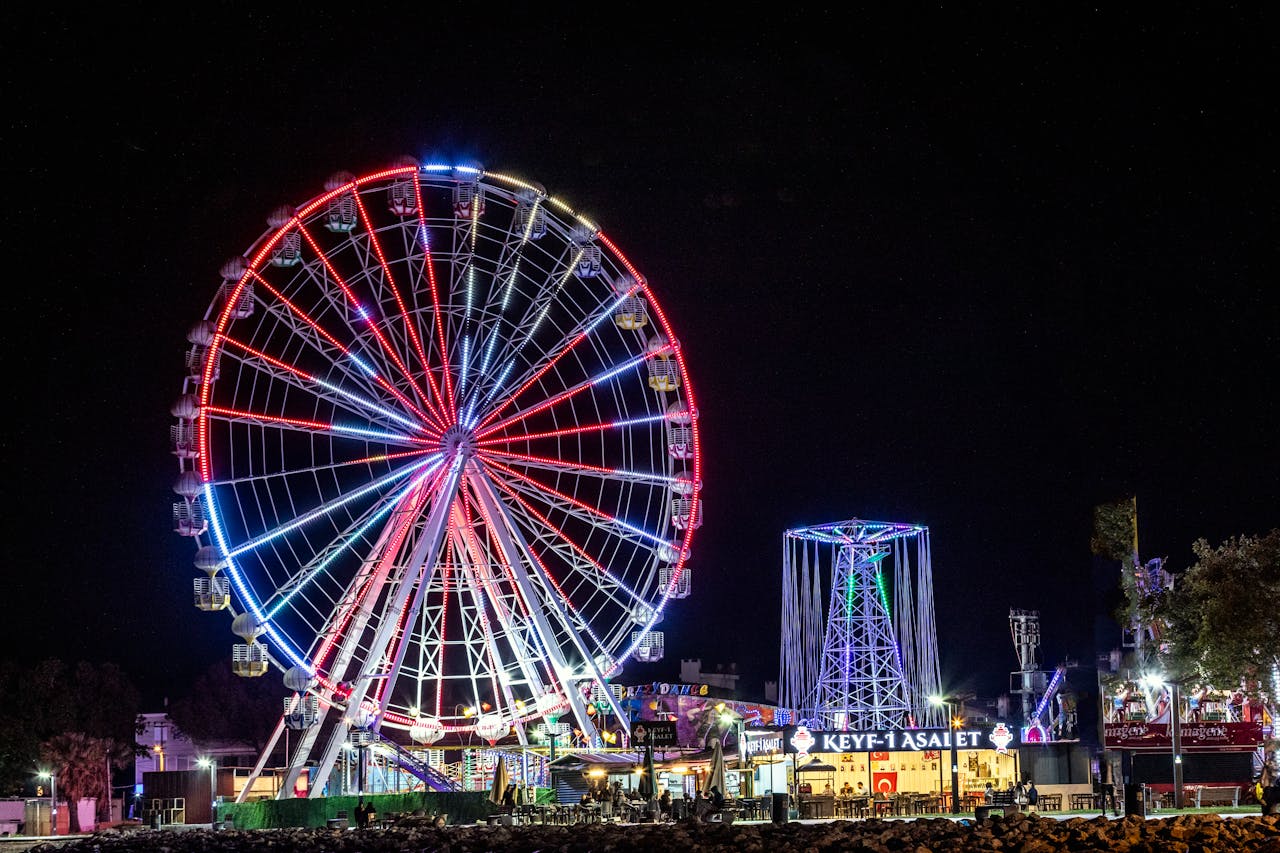 A brightly lit Ferris wheel glows in vibrant colors at an amusement park during the night.